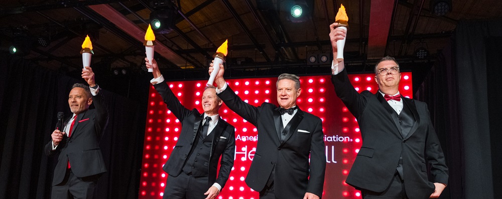 Four men in tuxedos holding up mock torches.